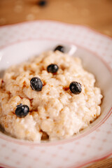 Close-up of creamy oatmeal porridge with blueberries in ceramic bowl. Soft light, warm tones and minimal composition create a calm healthy breakfast mood