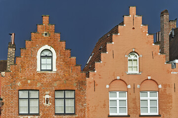 Two adjacent buildings in Bruges with stepped gable facades made of red brick.
