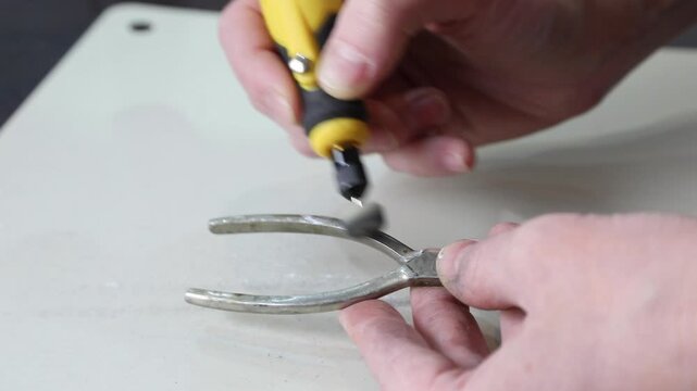 Man using a handheld rotary tool to restore vintage sugar tongs, polishing metal with attention to detail for antique preservation.