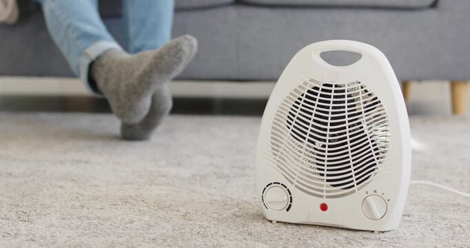 Heater warming cold home for cozy comfort. Portable electric heater on carpet, winter socks, quick spot heating, energy savings and budget control. Clear concept of home energy savings.