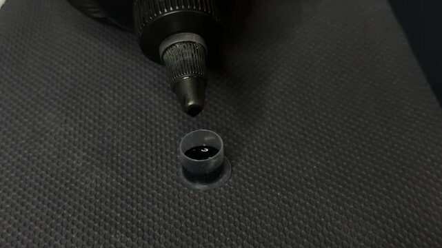 Tattoo ink being poured into a small plastic ink cap, with a tattoo machine nozzle visible in the frame.