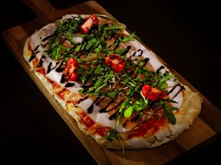 Gourmet flatbread pizza topped with prosciutto, fresh arugula, cherry tomatoes and balsamic glaze,...