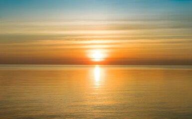 Golden sunset sky over calm sea water, orange sun reflection on ocean surface, peaceful nature landscape background, serene summer evening horizon, tranquil lake sunlight for travel and vacation.