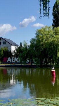 Calm waterway in Augustow, Poland, features reflective water with floating water lilies. A seagull perches on a red buoy. serene atmosphere of the canal area.