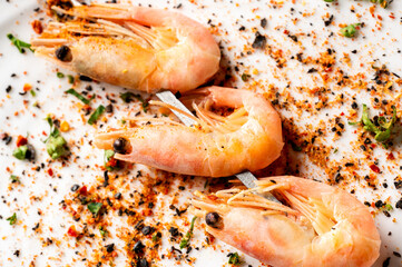  Three cooked prawns in their shells seasoned with red pepper flakes and herbs are presented in a close-up, high-angle shot on a white plate