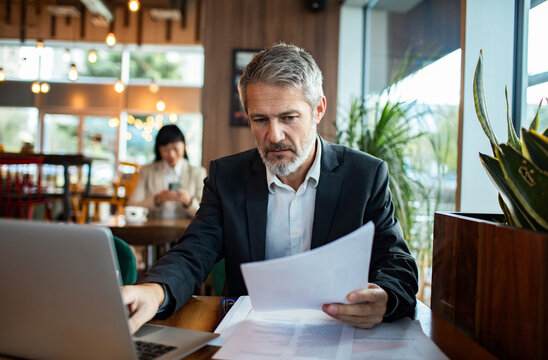 Mature businessman concentrating on paperwork in cafe