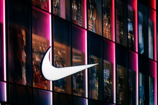 Shenzhen, China - December 8, 2025: Nike swoosh logo illuminated on vibrant neon-lit glass facade at night. Iconic sports brand symbol for athletic apparel, fitness and active lifestyle branding.