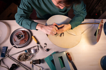 Craftsman upcycle master disassembling vintage electric lamp at workshop, man preparing item parts for repairing and inspection, taking out light bulb socket off lampshade, refurbishing and reuse.