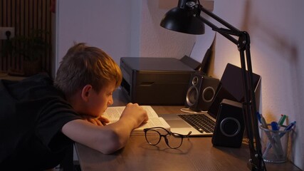 Diligent schoolboy study textbook under warm glow of desk lamp, preparing for an exam or completing homework assignments in cozy room during evening