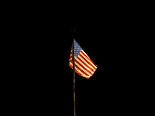 Illuminated American flag flying  on pole at night with black background