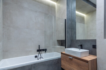 An elegant bathroom with a bathtub behind a glass partition and a wooden cabinet under the sink.