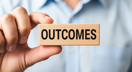 Businessman holding a wooden block with the word outcomes emphasizing results and final goals in business strategy