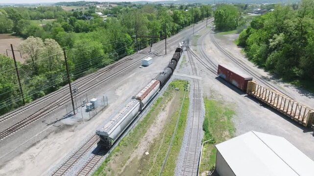 A vintage steam freight train makes its way backing up in yard performing switching operations moving steadily along the railway tracks in a peaceful countryside setting.