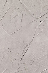 A white plaster wall with messy plasterer's strokes and black specks. Vertical photo