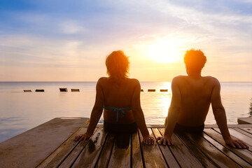 silhouette of couple sitting together in hotel with infinity swimming pool at sunset on sea beach, vacation travel