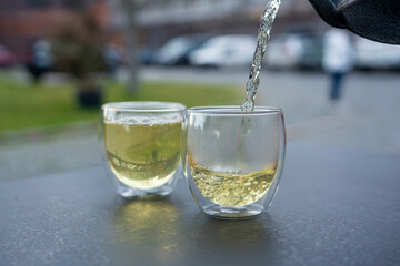 Pouring green tea into a glass from a metal kettle on blurred background, hot drink in teapot