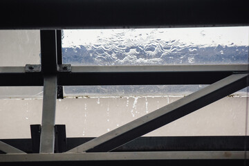 Rain falling on a transparent glass roof with water dripping from the dark metal support structure...