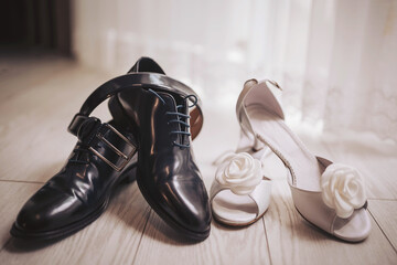 Different types of shoes sit on a wooden floor close to a window with soft light in a room designed for an event or celebration