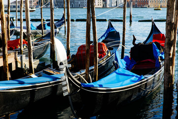 Venice, Italy - December 05, 2025: Gondolas with blue tarps are moored at a wooden dock in Venice, showcasing the iconic waterways and vibrant city life © HelgaQ