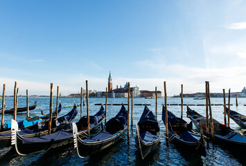 Venice, Italy - December 05, 2025: Gondolas lined up in the serene waters of Venice, showcasing iconic architecture and vibrant blue skies, capturing the essence of Italian culture and beauty © HelgaQ