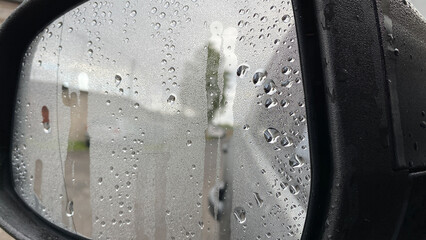 Fogged wet side mirror of the car, raindrops on the glass, close-up