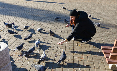 Woman feeds pigeons in a park while sitting on a bench during a sunny day