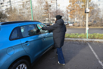 Person cleaning car windows in a parking lot during winter morning