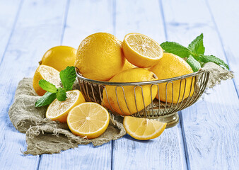 Świeże cytryny z listkami mięty w drucianym koszyku na niebieskim, drewnianym stole