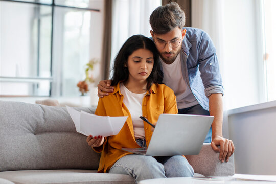 Household papers problem. Upset Indian couple looking at documents, doing paperwork together, sitting on sofa at home