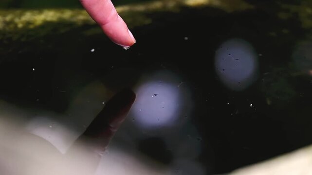 Close-up of finger creating ripples in dark water surface