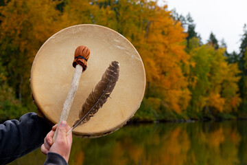 An image of a handmade leather meditation drum with brightly colored foliage and water reflection in the background.