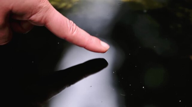 Close-up of finger touching water surface creating ripples