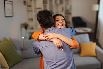 Happy Indian woman hugging her husband and holding house key on moving day, hindu couple embracing in their new home during relocation