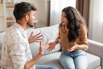 Breakup and divorce concept. Married Indian couple having fight, sitting on couch arguing, having...