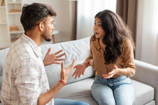 Breakup and divorce concept. Married Indian couple having fight, sitting on couch arguing, having dysfunctional relationship