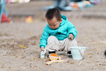 An Asian boy playing in a sandbox at a playground in winter