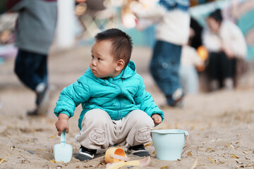 An Asian boy playing in a sandbox at a playground in winter
