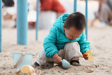 An Asian boy playing in a sandbox at a playground in winter