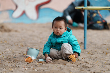 An Asian boy playing in a sandbox at a playground in winter
