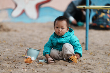 An Asian boy playing in a sandbox at a playground in winter