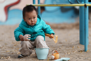 An Asian boy playing in a sandbox at a playground in winter