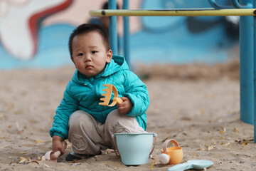 An Asian boy playing in a sandbox at a playground in winter