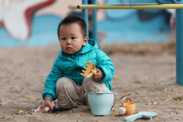An Asian boy playing in a sandbox at a playground in winter