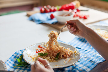 Close up of hands eating pasta with tomato sauce and basil on rustic plate. Homemade Italian pasta, warm kitchen light, comfort food concept. Woman twirling spaghetti. Candid, authentic lifestyle