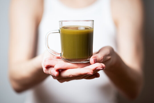 Kratom consumption concept:  female holds a ready to drink glass of green liquid, powdered kratom melted in hot water, kratom tea, close up photo, selective focus