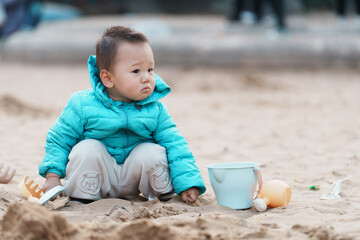 An Asian boy playing in a sandbox at a playground in winter