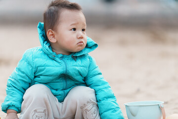 An Asian boy playing in a sandbox at a playground in winter
