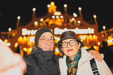 Happy senior couple enjoying a holiday stroll, smiling and embracing while taking a selfie at the festive dresden striezelmarkt during a beautiful winter night