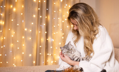 A young woman with Christmas decorations and her beloved cat at home preparing for Christmas