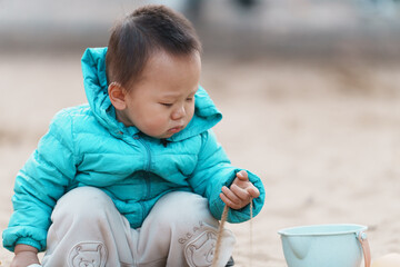 An Asian boy playing in a sandbox at a playground in winter